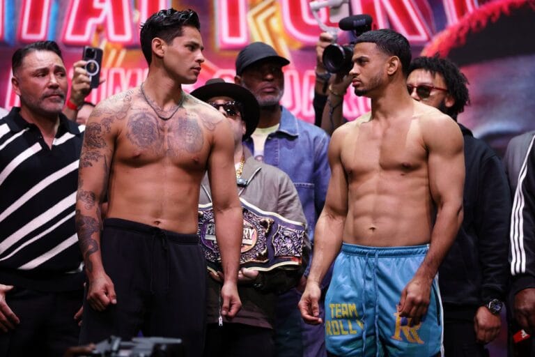 Ryan Garcia and Rolly Romero face off at weigh-in before Times Square boxing match, with title belt and promoters in background.